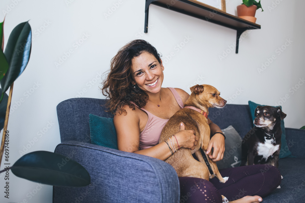 Obraz premium Portrait of happy Caucasian woman in casual clothing hug favourite dogs feeling love emotions during daily routine in home living room, cheerful hipster girl 20s take care of cute pets in collar