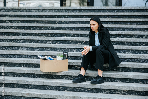 A frustrated woman sits on the stairs outside, feeling the weight of her jobless situation and the struggle to make ends meet. Depressed Woman with Cardboard Box on Stairs photo