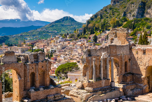 Taormina on Sicily, Italy. Ruins of ancient Greek theater, mount Etna covered with clouds. Taormina old town and mountains in background. Popular touristic destination on Sicily