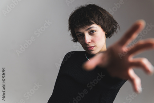 Medium shot of a pretty female model hodling her hand stretched forward and looking into the camera. Gray background. High quality photo photo