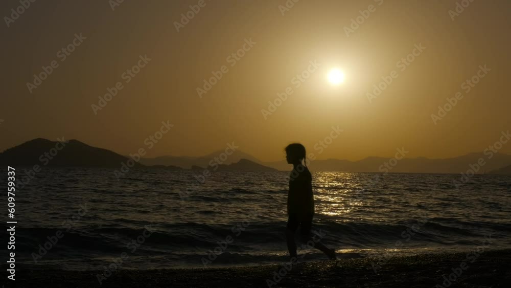 Resting child promenade silhouette by sea. A happy girl silhouette have fun and walk along the beach by the sea waves in the evening. Resting child promenade silhouette by sea. A happy girl silhouette have fun and walk along the beach by the sea waves in the evening.