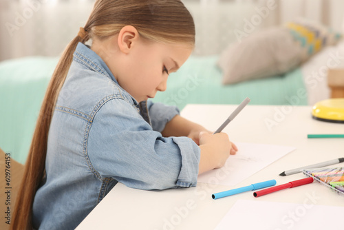 Cute little girl drawing with marker at desk in room. Home workplace