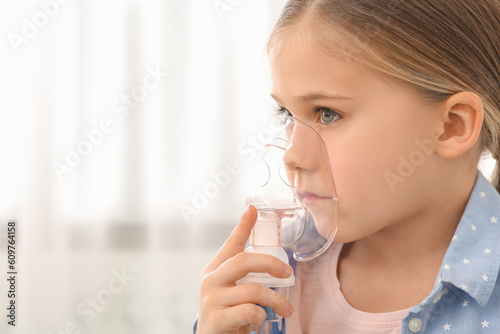 Sick little girl using nebulizer for inhalation indoors