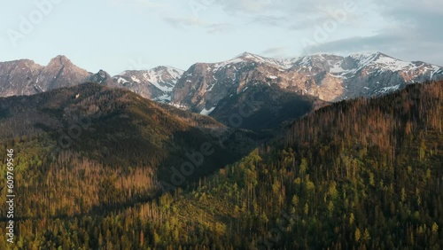Stunning view high mountain peaks covered with snow lit with warm sunrise or sunset light, aerial drone shot of beautiful mountains and hills, spring season early morning, mountain range golden hour