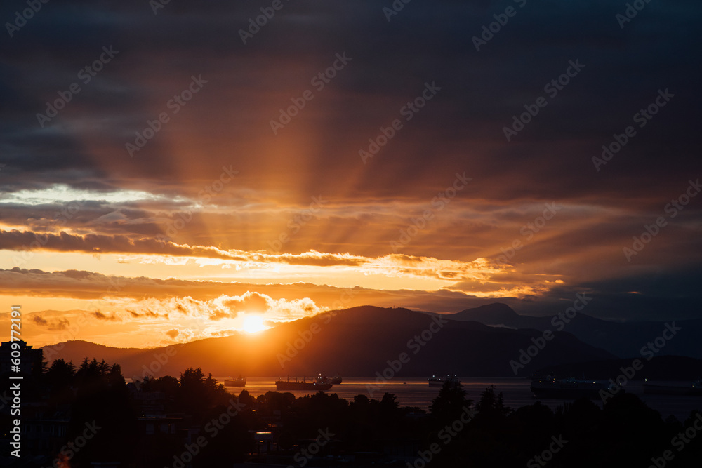 The evening sun drops behind the mountains behind English Bay, Vancouver, BC