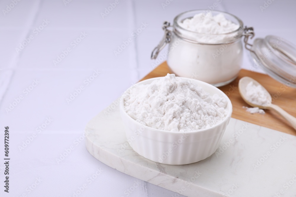 Bowl, spoon and glass jar of natural starch on white tiled table. Space for text