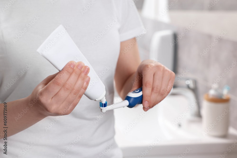 Woman squeezing toothpaste from tube onto electric toothbrush in bathroom, closeup Woman squeezing toothpaste from tube onto electric toothbrush in bathroom, closeup