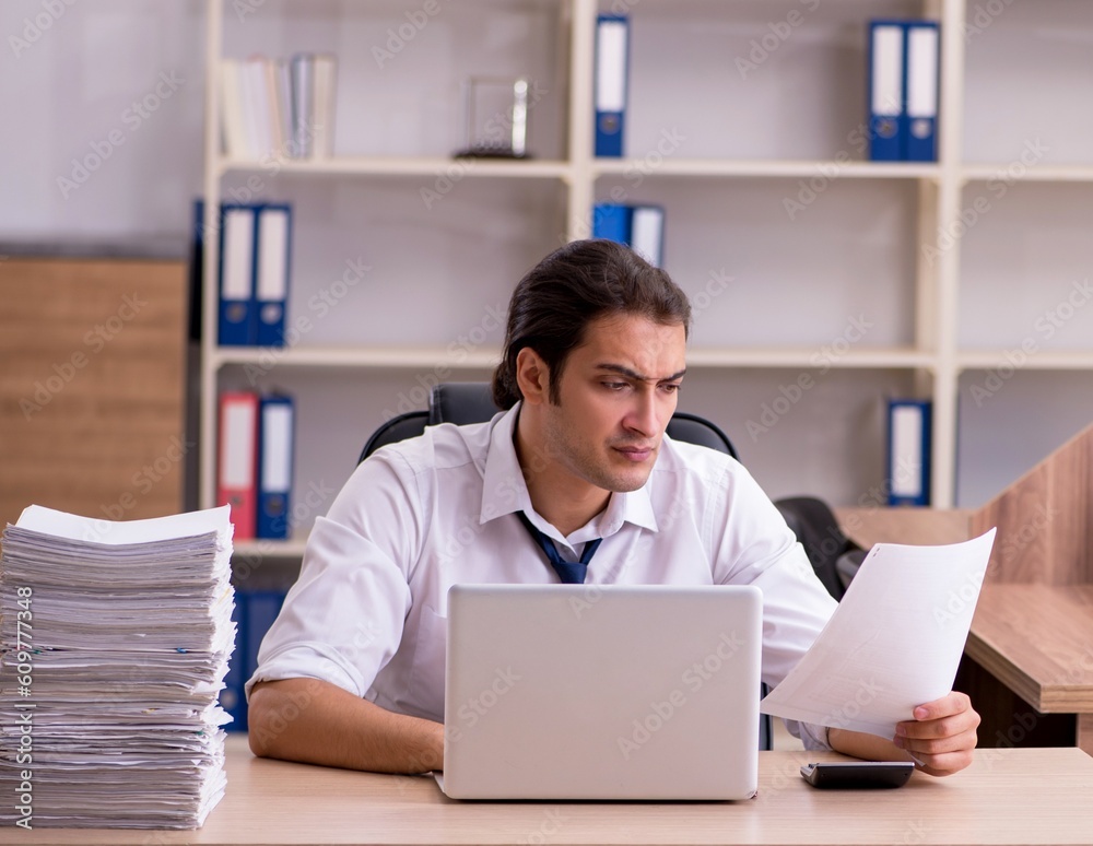 Young male employee unhappy with excessive work in the office Young male employee unhappy with excessive work in the office