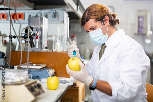Portrait of skilled man lab technician working in food testing laboratory, testing apple on pesticides and chemicals residues to ensure quality of product