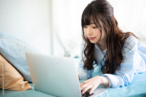 ベッドに寝転がってノートパソコンを見ている女性 photo