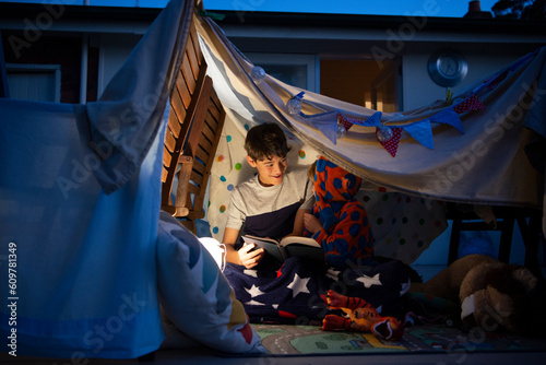 シーツで作ったテントの中で本を読んでいる兄弟 photo