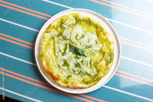 香り高いバジルソースととろけるチーズが食欲をそそるジェノベーゼピッツァ。中央に添えられたフレッシュバジルがアクセントの、ランチやパーティーに最適な本格イタリアン料理素材です。 | Genovese pizza with rich basil sauce and melted cheese on a white plate.