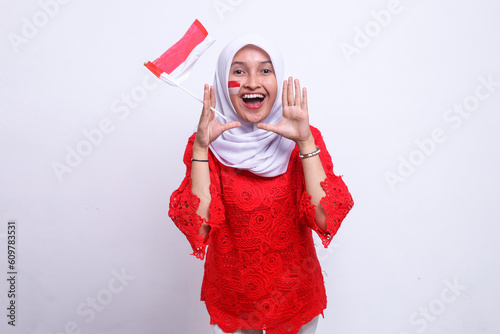 Happy excited Indonesian woman holding Indonesia flag and shout announce to camera isolated over white background. Indonesia Independence Day celebration.  photo