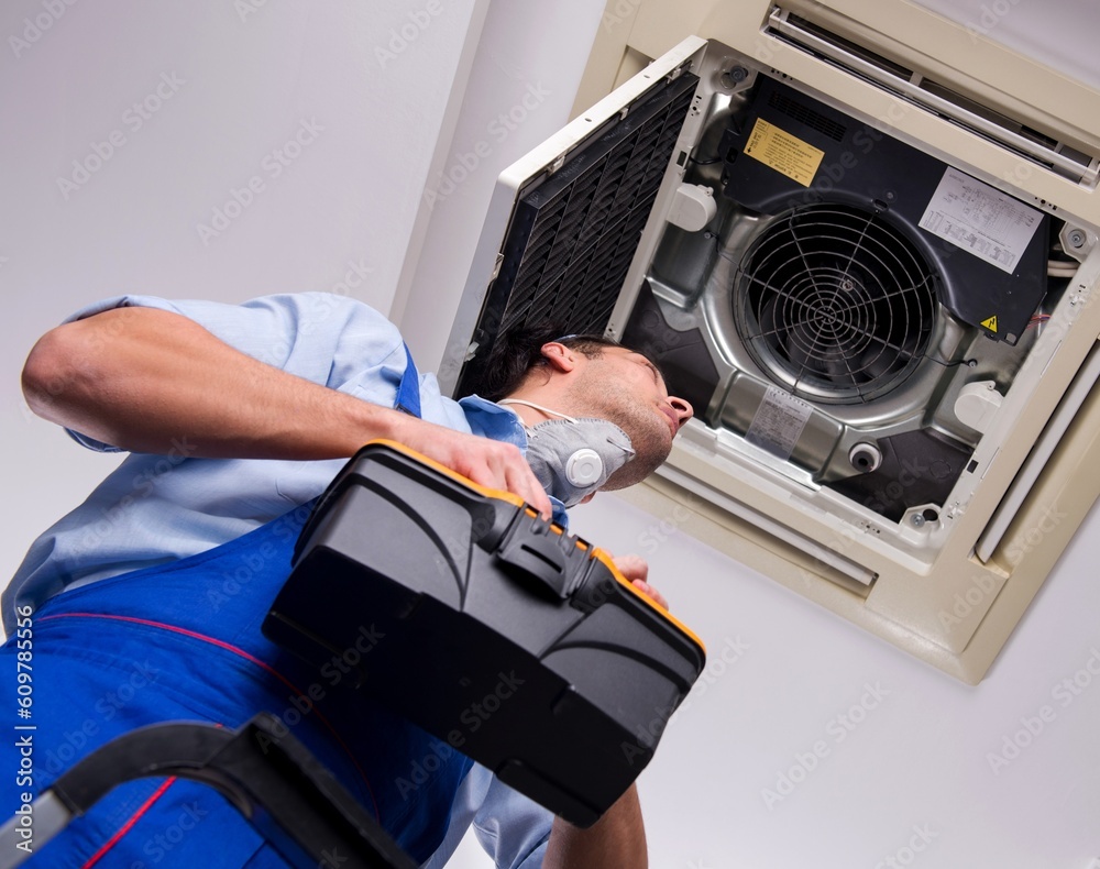 Young repairman repairing ceiling air conditioning unit