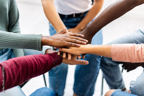 Young group of people sitting in circle stacking hands. Multiracial friends putting their hands together showing unity, support and community.