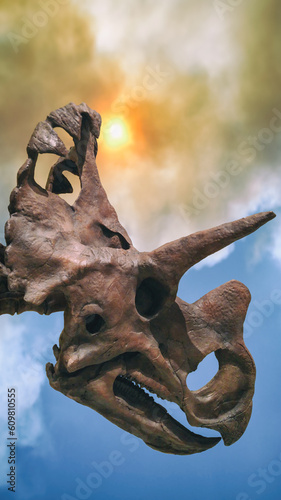 Φωτογραφία A triceratops dinosaur fossil skull against a background of smoke and sun, extinction event