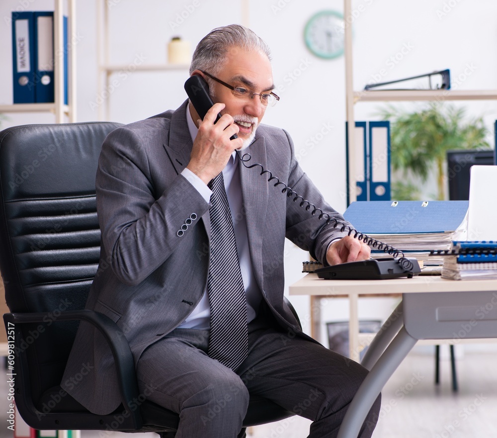 Old male employee using phone in the office Old male employee using phone in the office