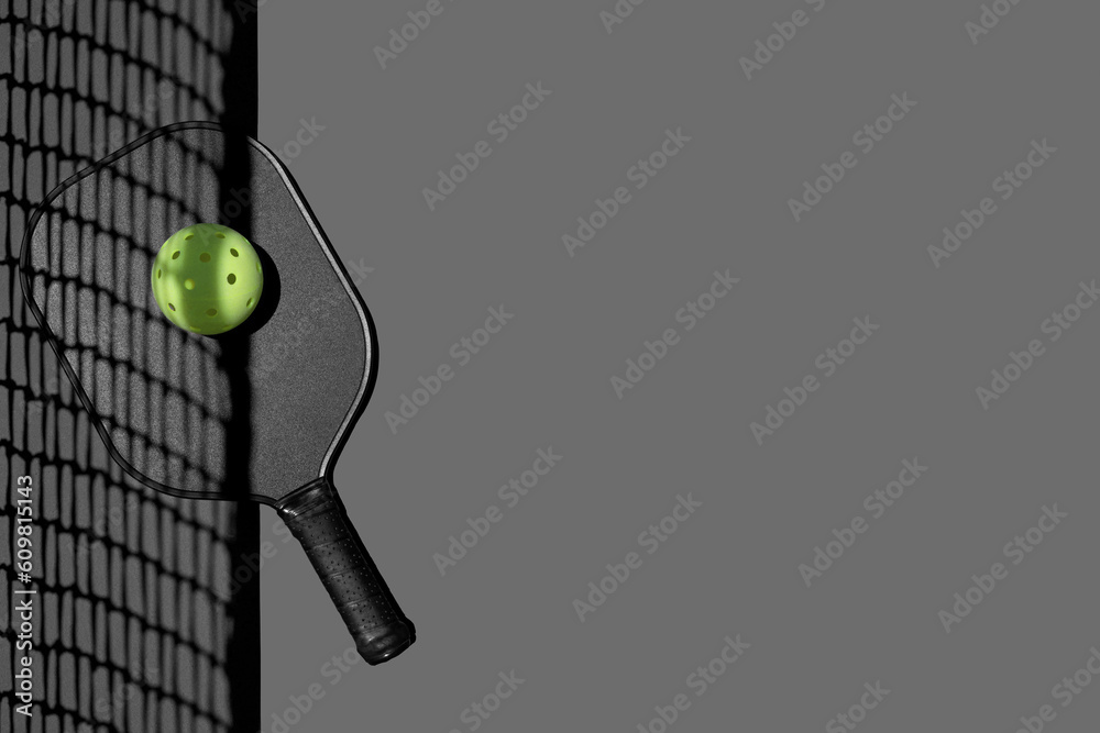 Flatlay of a pickleball paddle and ball on gray