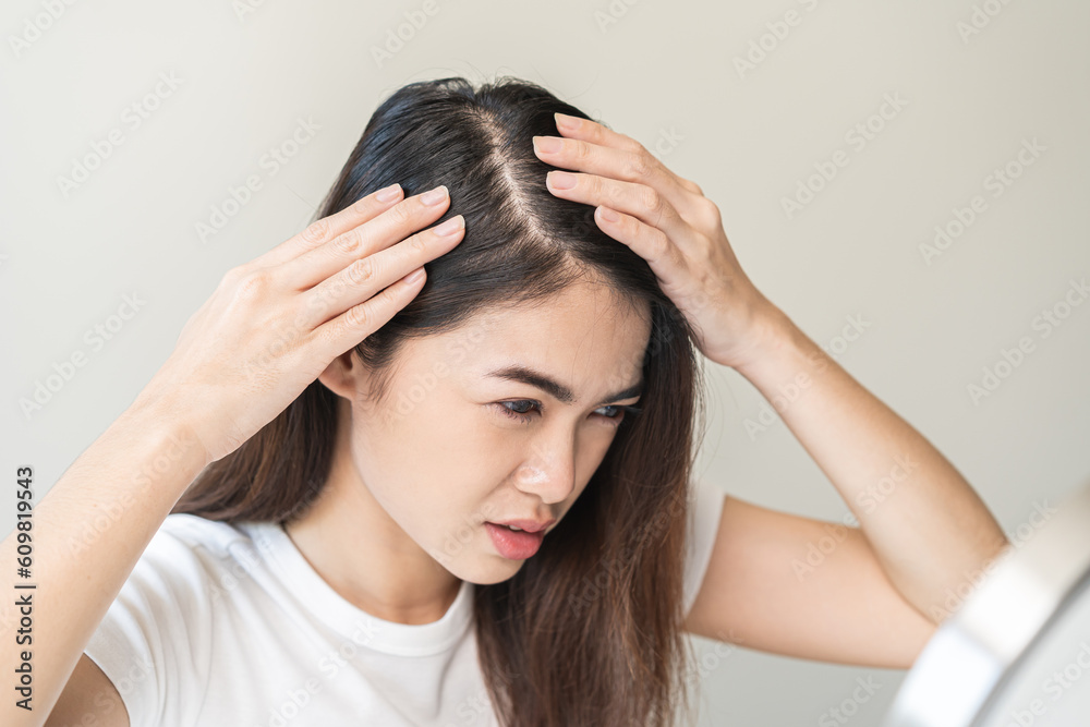 Damaged Hair symptom, face serious asian young woman, girl worry about balding, looking at scalp in mirror, hand in break into front hair loss, thin problem. Health care treatment for beauty concept. Damaged Hair symptom, face serious asian young woman, girl worry about balding, looking at scalp in mirror, hand in break into front hair loss, thin problem. Health care treatment for beauty concept.
