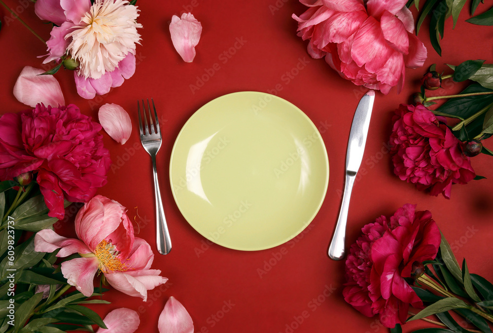 Festive table setting with green plate, cutlery and pink peonies on red table. Festive table setting with green plate, cutlery and pink peonies on red table.