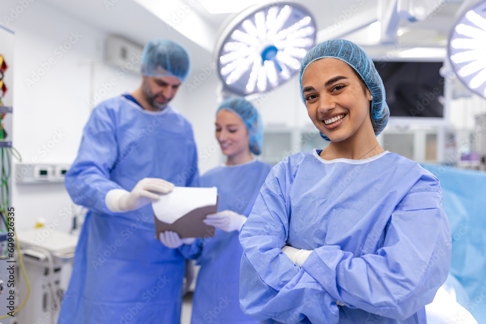 Obraz premium Portrait of female woman nurse surgeon OR staff member dressed in surgical scrubs gown mask and hair net in hospital operating room theater making eye contact smiling pleased happy looking at camera