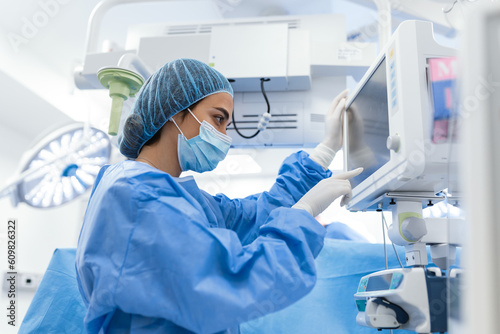 Portrait of a young female doctor in scrubs and a protective face mask preparing an anesthesia machine before an operation
