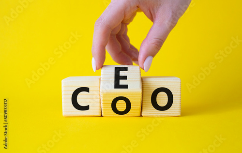 CEO and COO symbol. Businessman hand turns wooden cubes and changes word CEO to COO. Beautiful yellow background. CEO and COO and business concept. Copy space