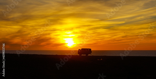 Silhouette of traveler camper on ocean coast at sunset