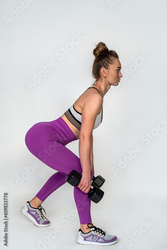 young woman squats with dumbbells to pump the muscles of the buttocks isolated on background.