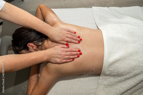 Woman masseur doing massage back of her female client lying face down on table at spa salon
