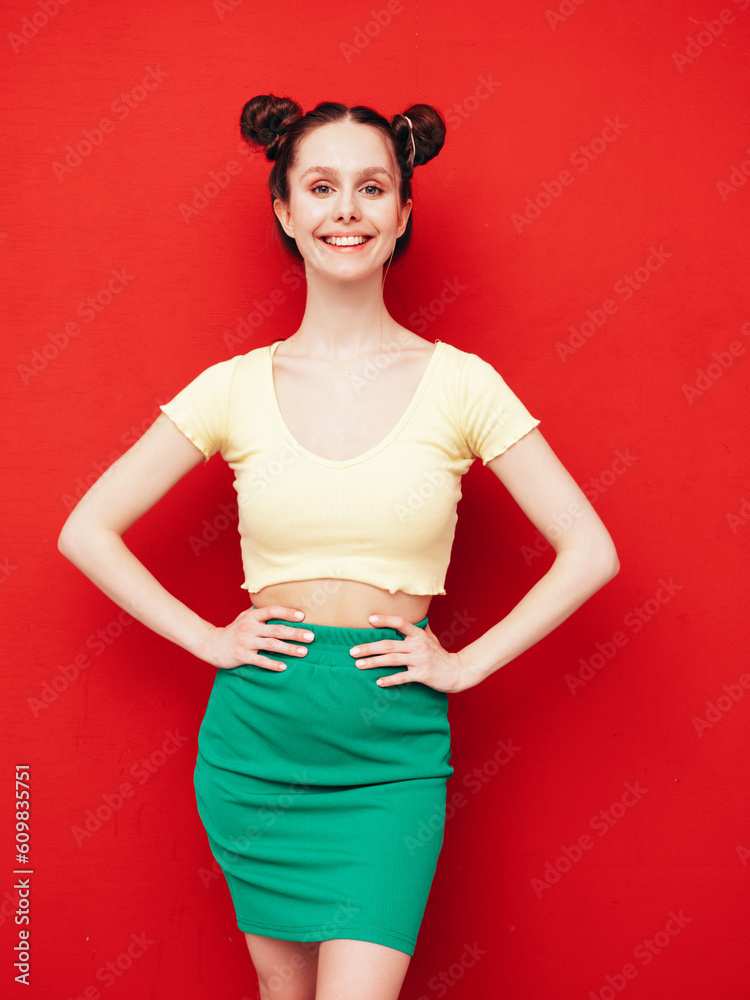 Young beautiful smiling female in trendy summer yellow t-shirt and green skirt. Carefree woman with two horns hairstyle posing near red wall in studio. Positive model having fun. Cheerful and happy Young beautiful smiling female in trendy summer yellow t-shirt and green skirt. Carefree woman with two horns hairstyle posing near red wall in studio. Positive model having fun. Cheerful and happy