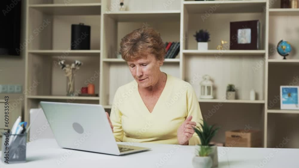 Seated at the table, an elderly woman engages in a lively video call conversation. Her face is filled with various emotions as she passionately conveys her thoughts, accompanied by animated gestures. Seated at the table, an elderly woman engages in a lively video call conversation. Her face is filled with various emotions as she passionately conveys her thoughts, accompanied by animated gestures.