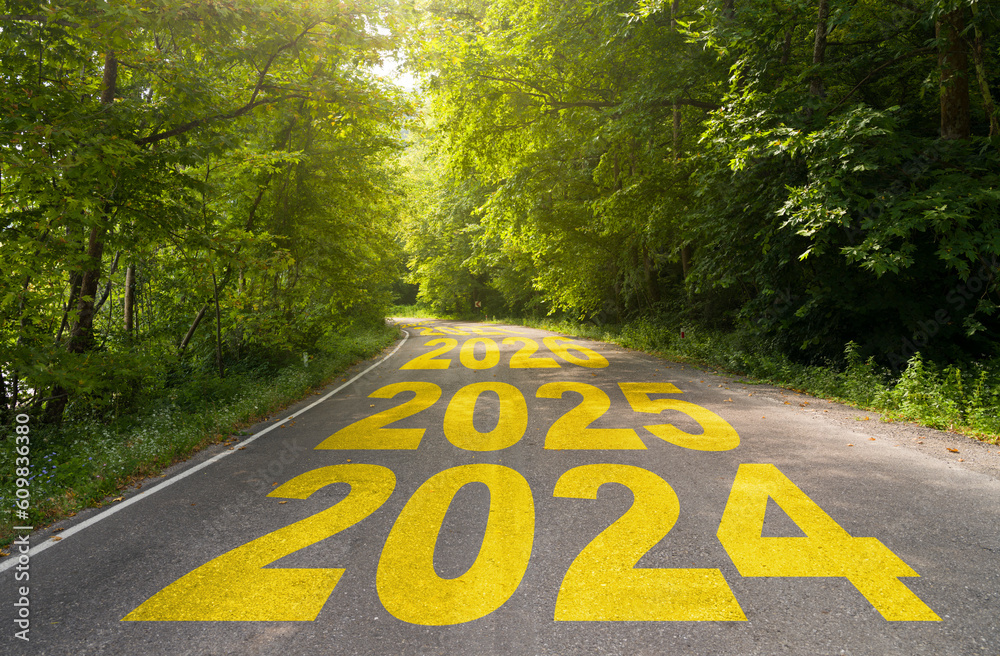 The word 2024 written on road in the middle of empty asphalt forest road at sunrise. Idea