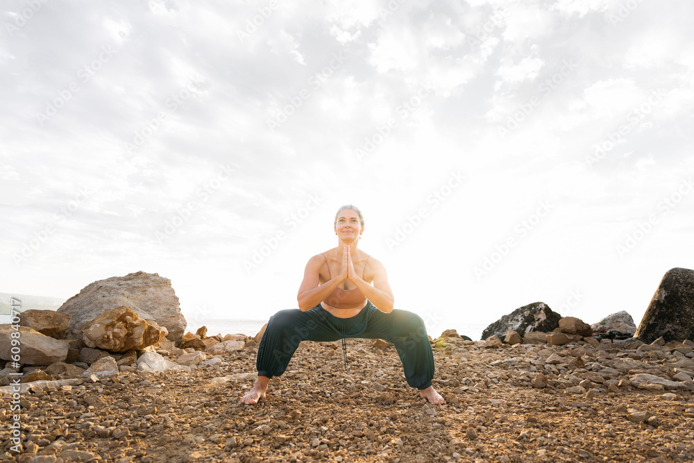 Woman practicing yoga in squatting position at beach Woman practicing yoga in squatting position at beach