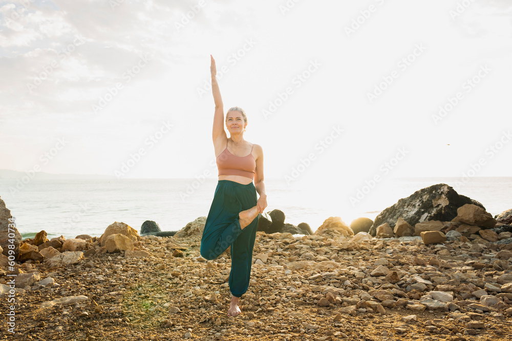 Woman practicing yoga standing on one leg in front of sky at beach Woman practicing yoga standing on one leg in front of sky at beach