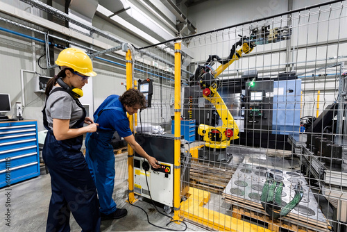 Maintenance engineers operating robotic arm in modern factory