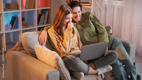 Family internet. Video watching. Happy mother daughter laughing sitting couch looking funny film on laptop enjoying leisure together home interior.