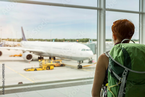 Woman with backpack looking at plane through window at airport photo