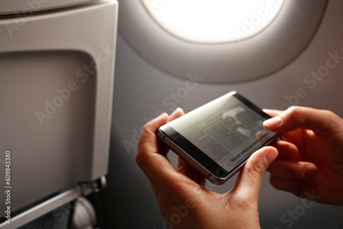 Hands of woman holding smart phone with news article on display in airplane photo