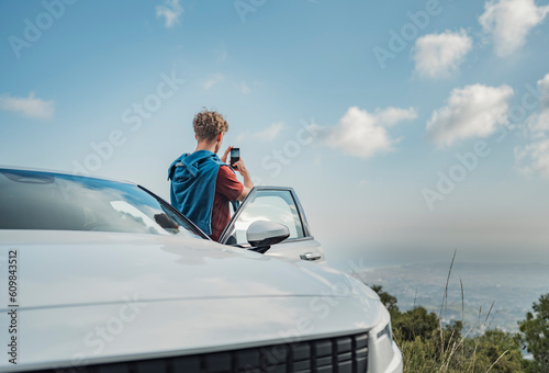 Man photographing with mobile phone standing by white car photo