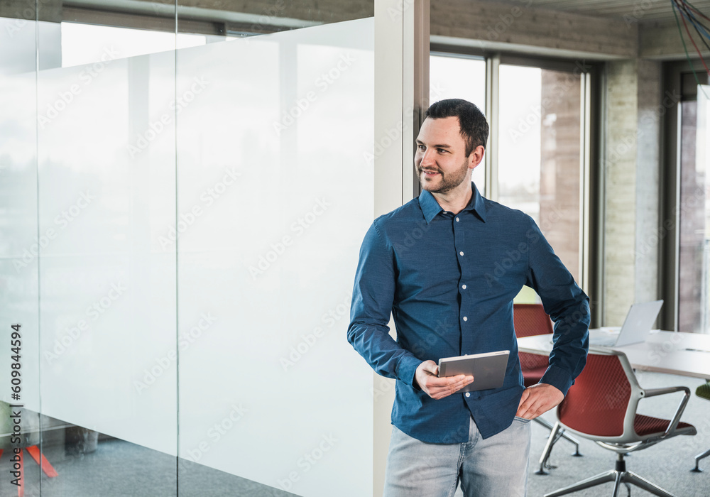 Businessman with tablet PC standing by glass door at workplace Businessman with tablet PC standing by glass door at workplace