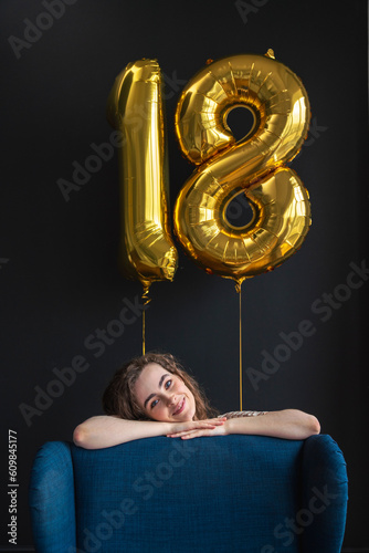 Young woman leaning on chair with number 18 balloon on black backdrop photo