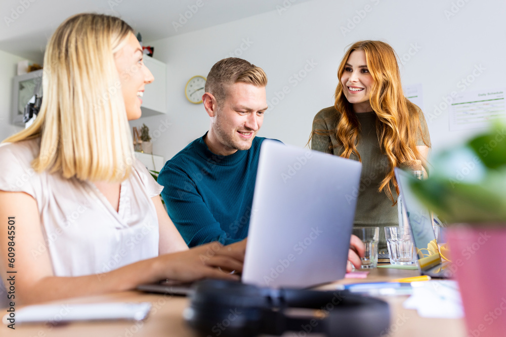 Smiling businesswoman talking to colleagues at desk in office Smiling businesswoman talking to colleagues at desk in office