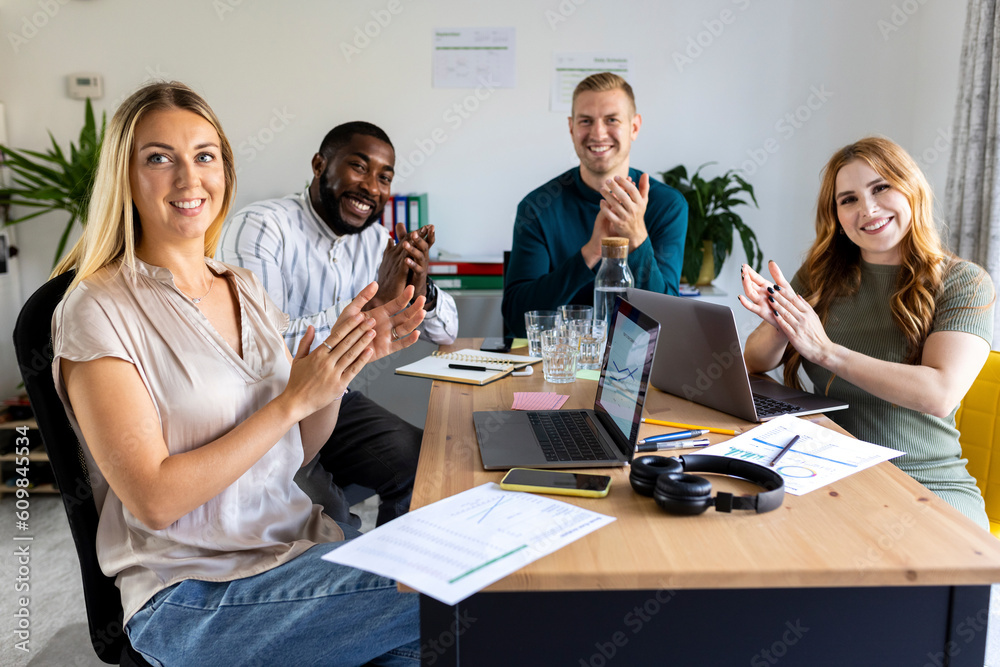 Smiling businessmen and businesswomen applauding at desk in meeting Smiling businessmen and businesswomen applauding at desk in meeting