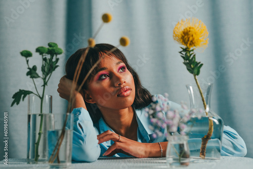 Thoughtful woman sitting at table with flowers in front of blue backdrop photo