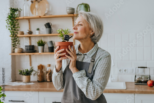 Mature woman smelling rosemary plant in kitchen at home