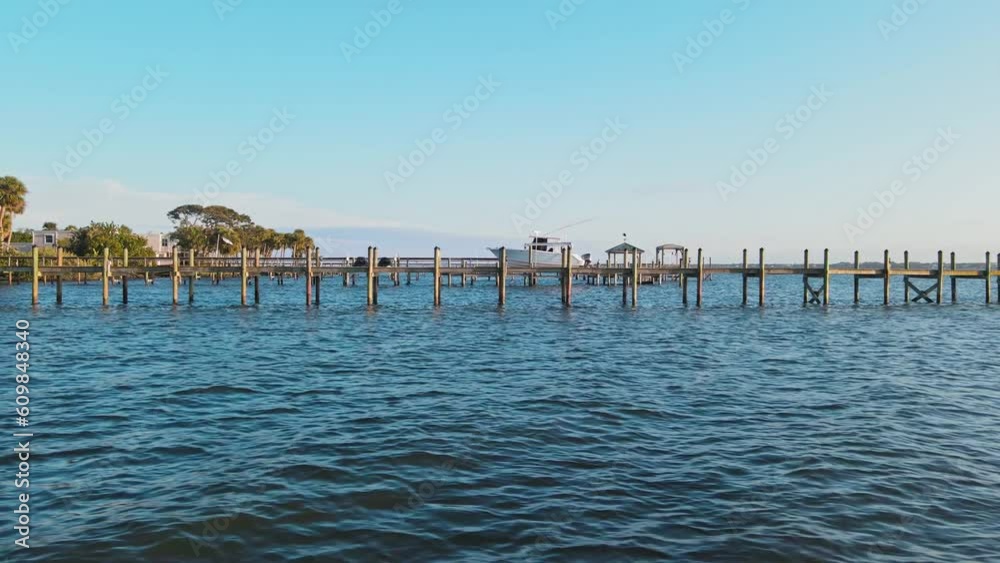 A horizontal shot of a pier starting at the shore that has palm trees and pretty landscaping and going out into the ocean water at sunset A horizontal shot of a pier starting at the shore that has palm trees and pretty landscaping and going out into the ocean water at sunset