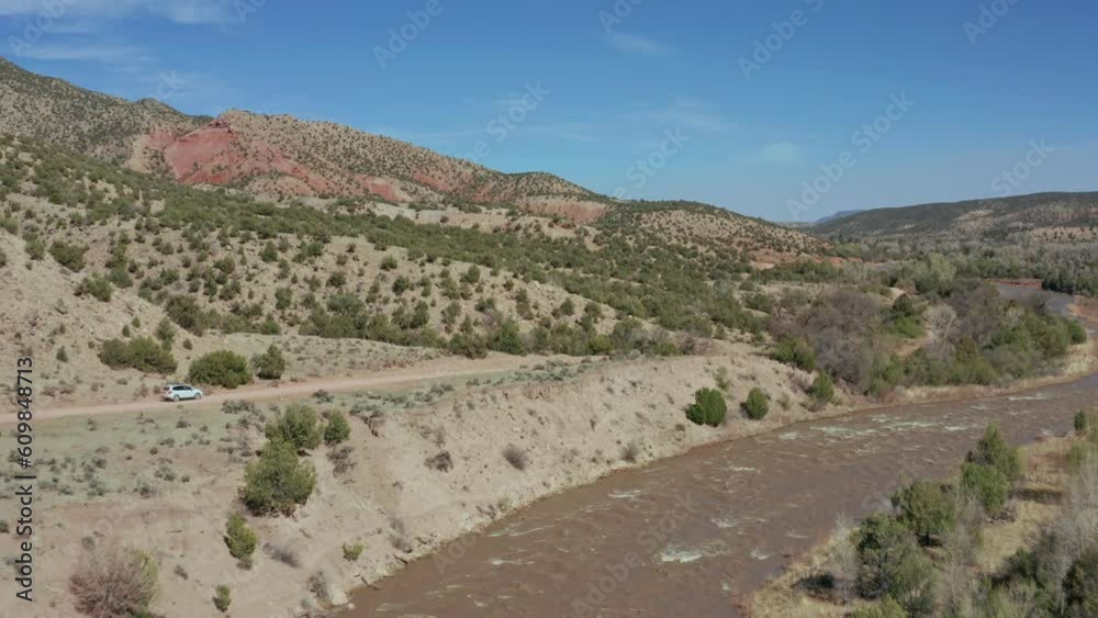 Aerial view following car along dirt road by river in desert landscape Aerial view following car along dirt road by river in desert landscape