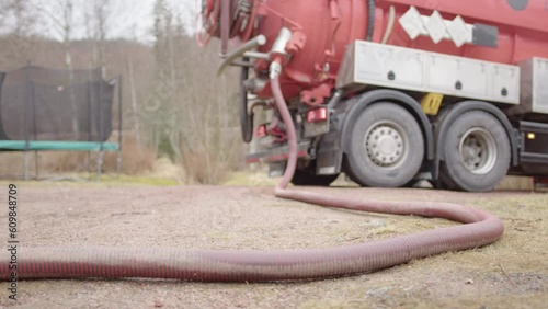 Red septic pumping truck pumps wastewater effluent through sewage suction hose