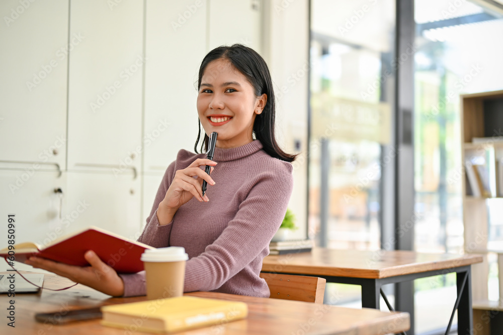 Attractive Asian female college student sitting in a co-working space with her school stuff. Attractive Asian female college student sitting in a co-working space with her school stuff.
